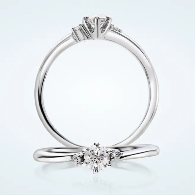 繊細でしなやかなウェーブラインに、センターの 0.2ct 天然ダイヤモンドを 6本爪で留めたエンゲージリングです。両サイドにメレダイヤモンド 2石（計0.02ct）を添えています。